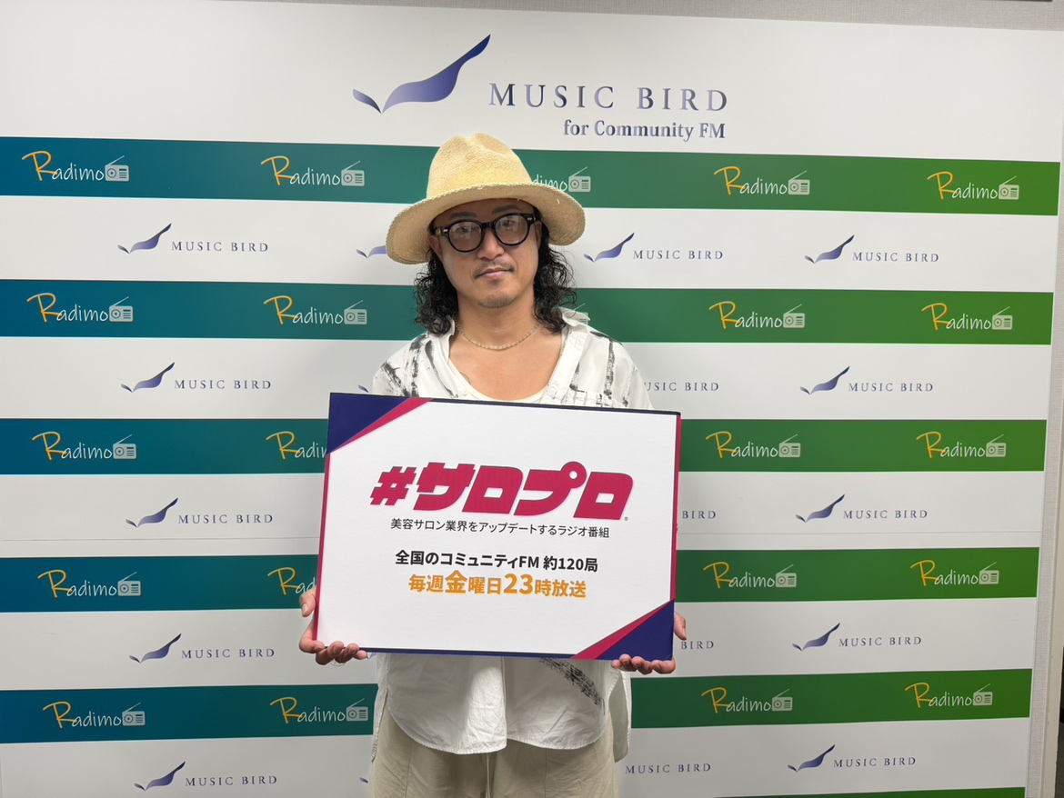 「サロプロ ラジオ」のボードを持つ取締役副社長 山野井宏明